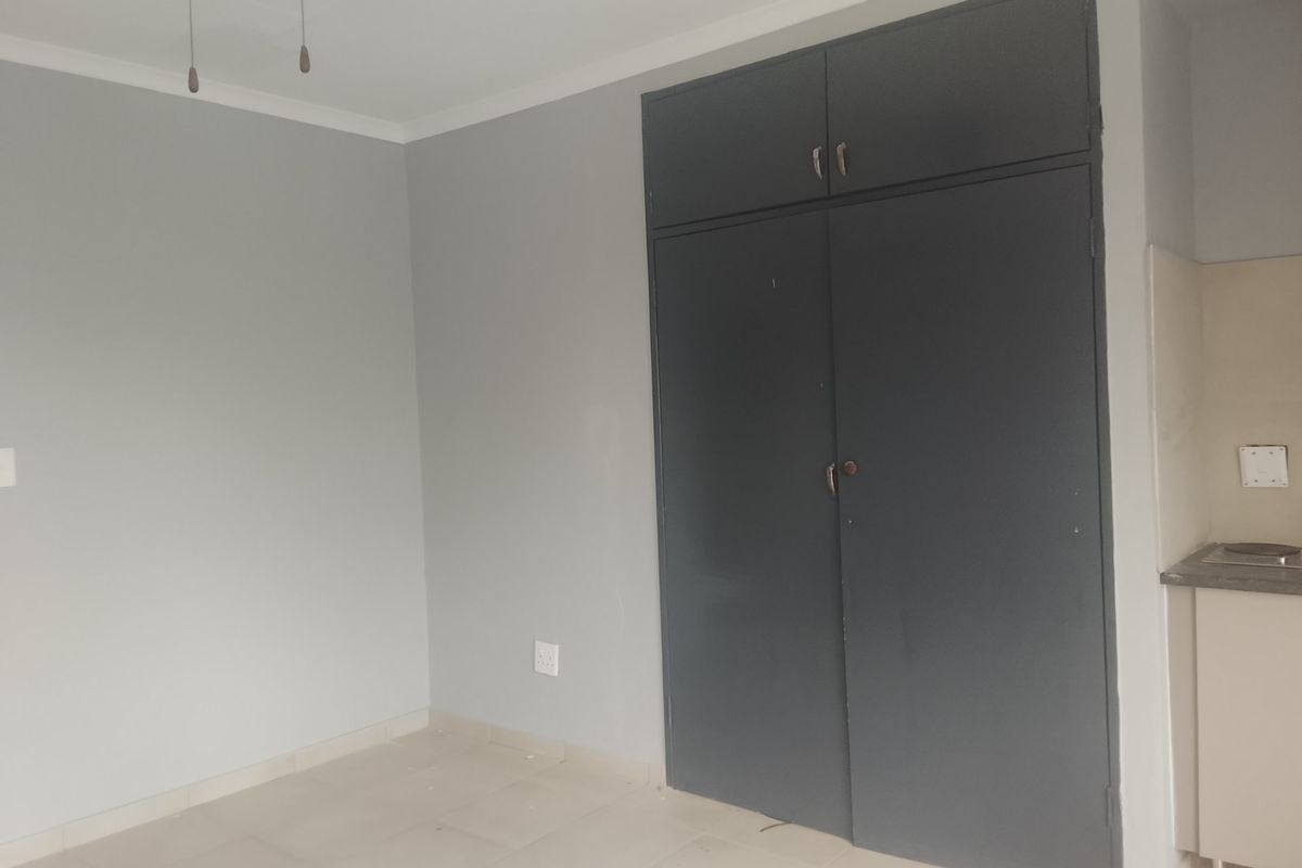 A clean, empty bedroom featuring neutral grey walls, tiled flooring, and dark built-in cupboards with overhead storage.