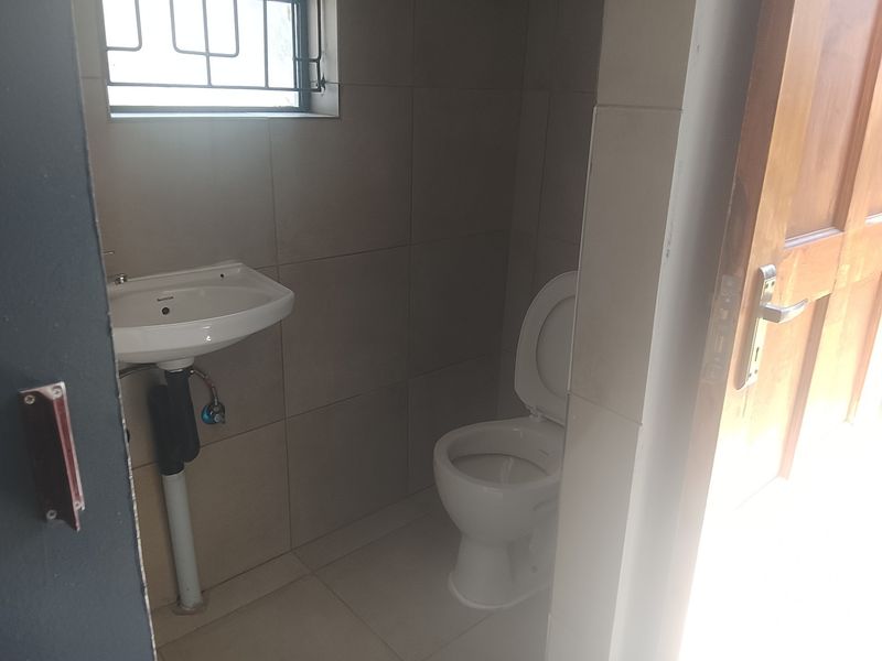 A compact guest bathroom featuring tiled walls, a wall-mounted basin, and a standard toilet, accessible via a timber door.
