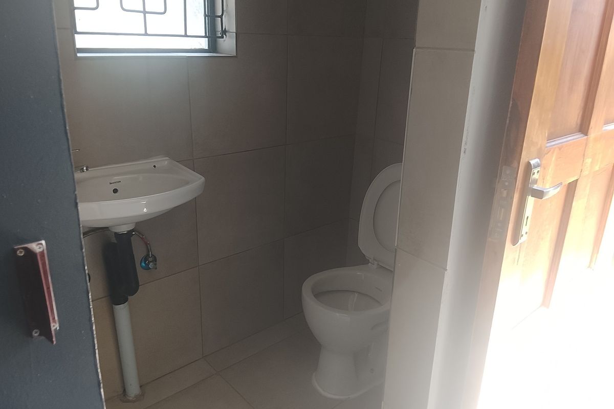 A compact guest bathroom featuring tiled walls, a wall-mounted basin, and a standard toilet, accessible via a timber door.