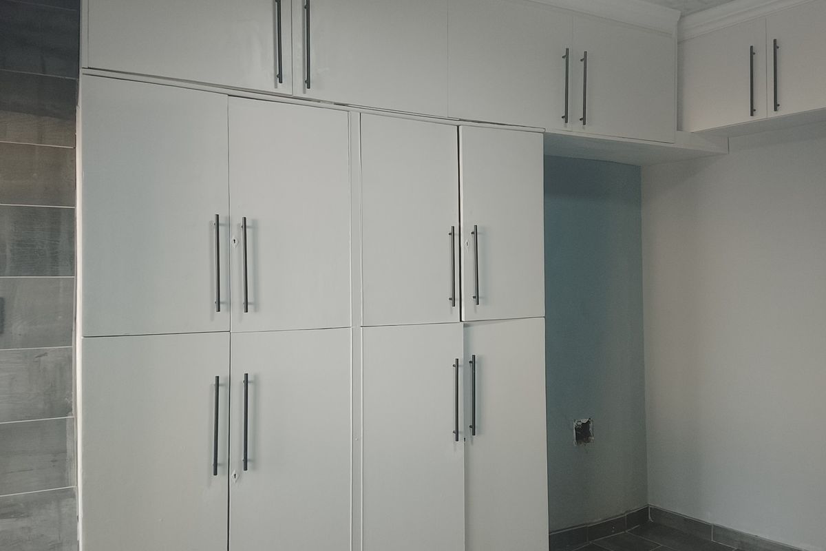A kitchen area featuring white built-in cabinetry with modern handles and tiled flooring, currently vacant and awaiting final finishes.