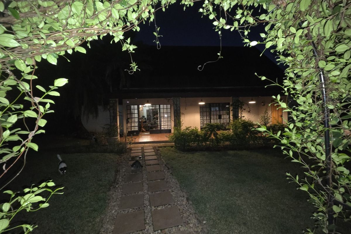 Night view of the rear exterior featuring a paved garden walkway leading to a covered patio area with exterior lighting.
