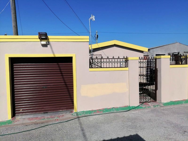 Front exterior view of the property featuring a roller garage door, perimeter wall with metal fencing, and a secure pedestrian gate.
