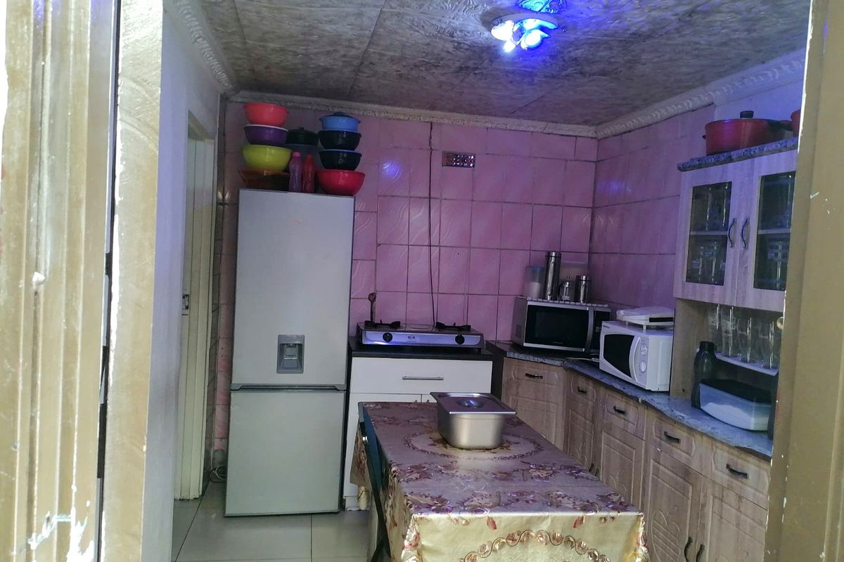 A compact kitchen featuring dated wall tiles, built-in cabinetry, and tiled flooring, offering potential for a modern renovation.