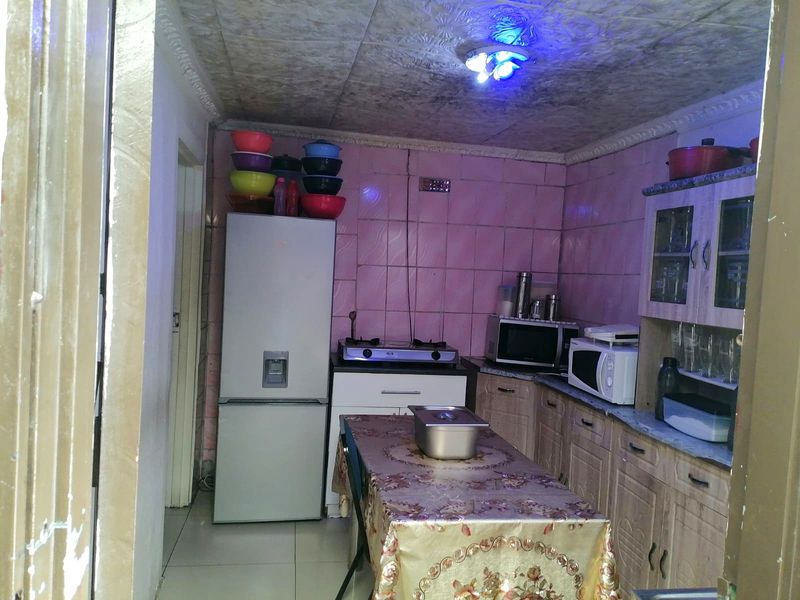 A compact kitchen featuring dated wall tiles, built-in cabinetry, and tiled flooring, offering potential for a modern renovation.