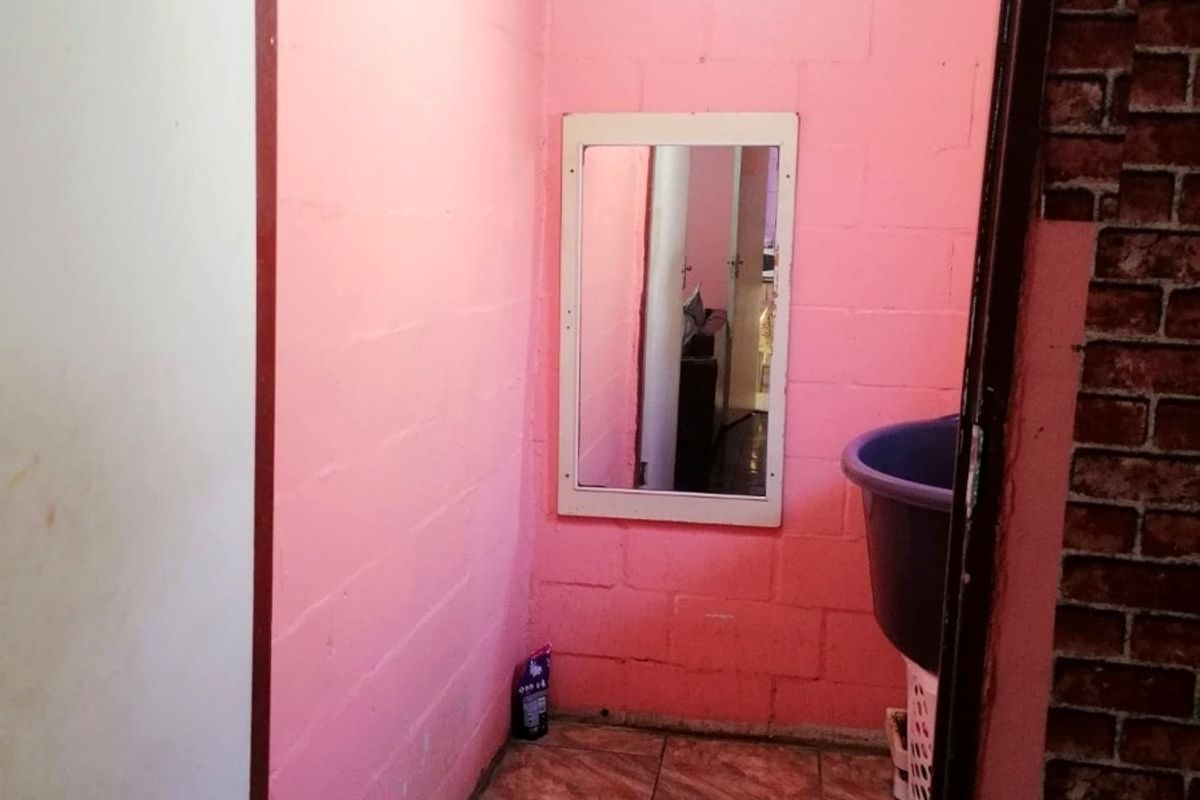 A small bathroom featuring tiled flooring and pink painted blockwork walls, currently requiring significant cosmetic updates and finishing work.
