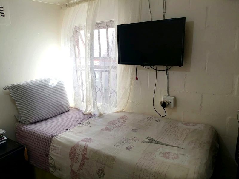 A compact bedroom featuring a window with security bars and wall-mounted electrical infrastructure.