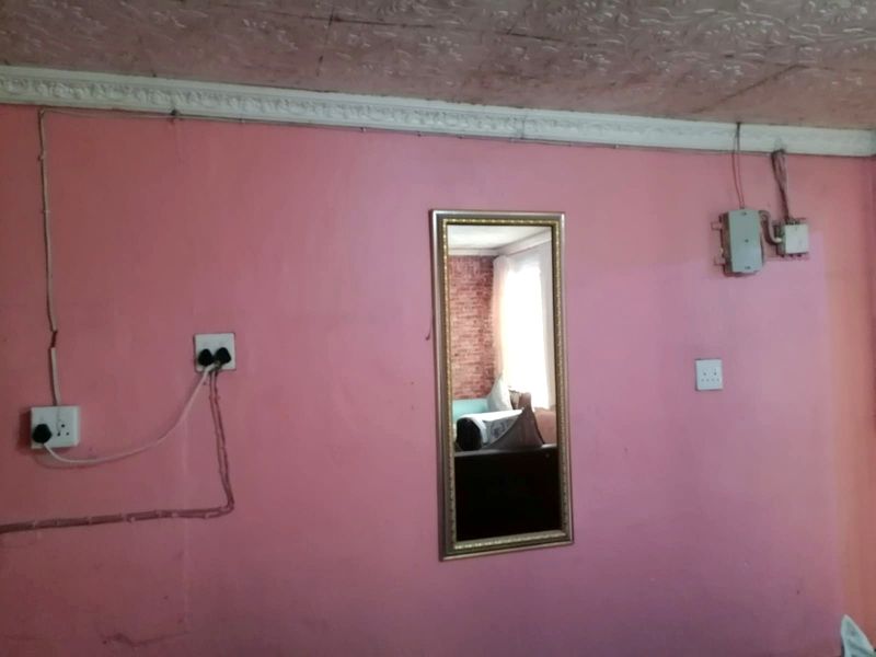 A bedroom interior featuring pink walls, textured ceiling, and visible surface-mounted electrical wiring and outlets.