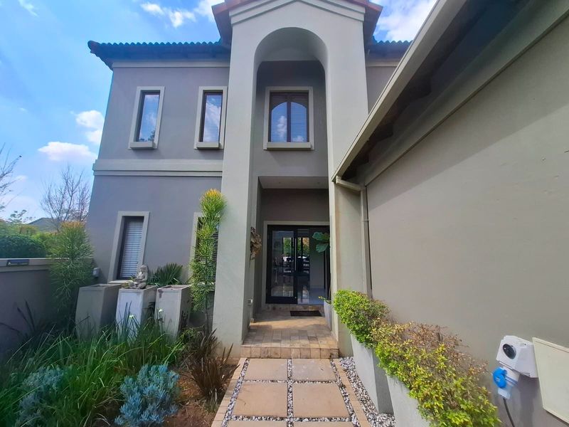A well-maintained double-storey house entrance featuring an arched portico, tiled walkway, and landscaped built-in planters.