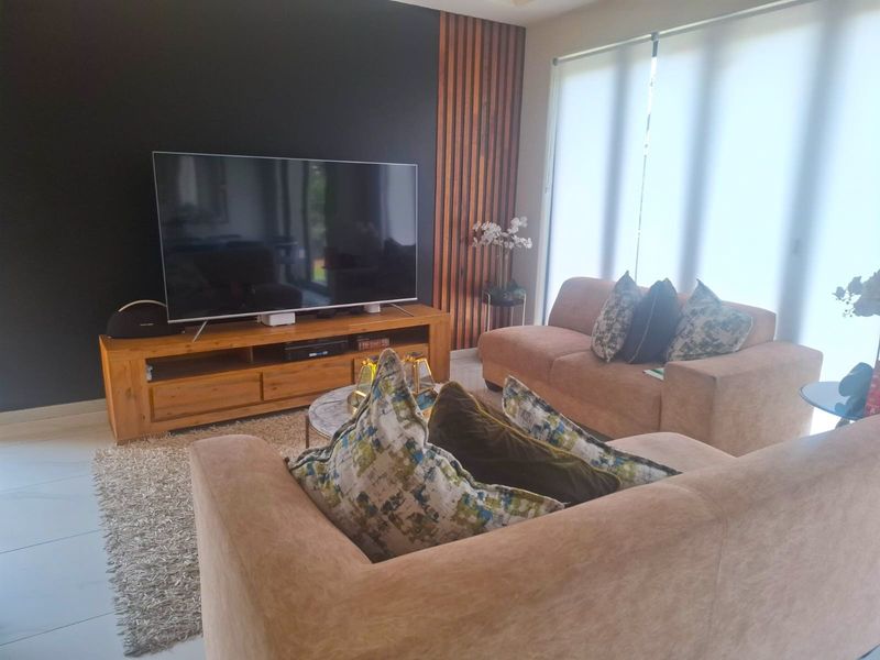 A modern living room featuring a striking black feature wall with timber slat accents, tiled flooring, and large windows with roller blinds.