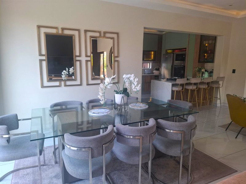 Open plan dining area flowing into a modern kitchen featuring a central island, built-in appliances, and polished tiled flooring.