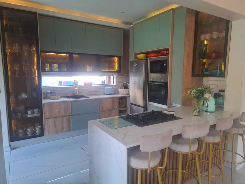 Modern kitchen featuring sage green and wood-grain cabinetry, stone countertops, a central island with a gas hob, and integrated appliances.