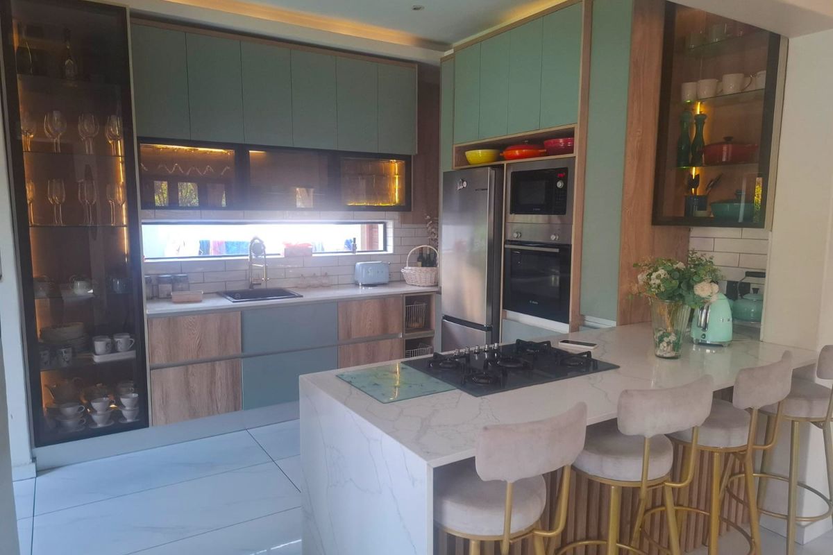 Modern kitchen featuring sage green and wood-grain cabinetry, stone countertops, a central island with a gas hob, and integrated appliances.