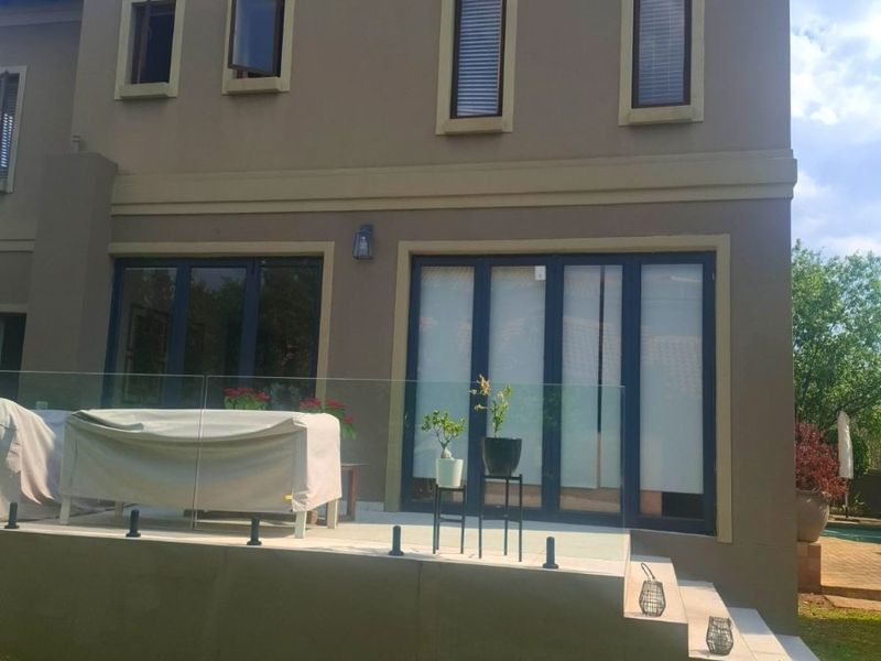 Rear elevation of a two-story house featuring a tiled patio, glass balustrade, and modern aluminium-framed doors leading to the garden.