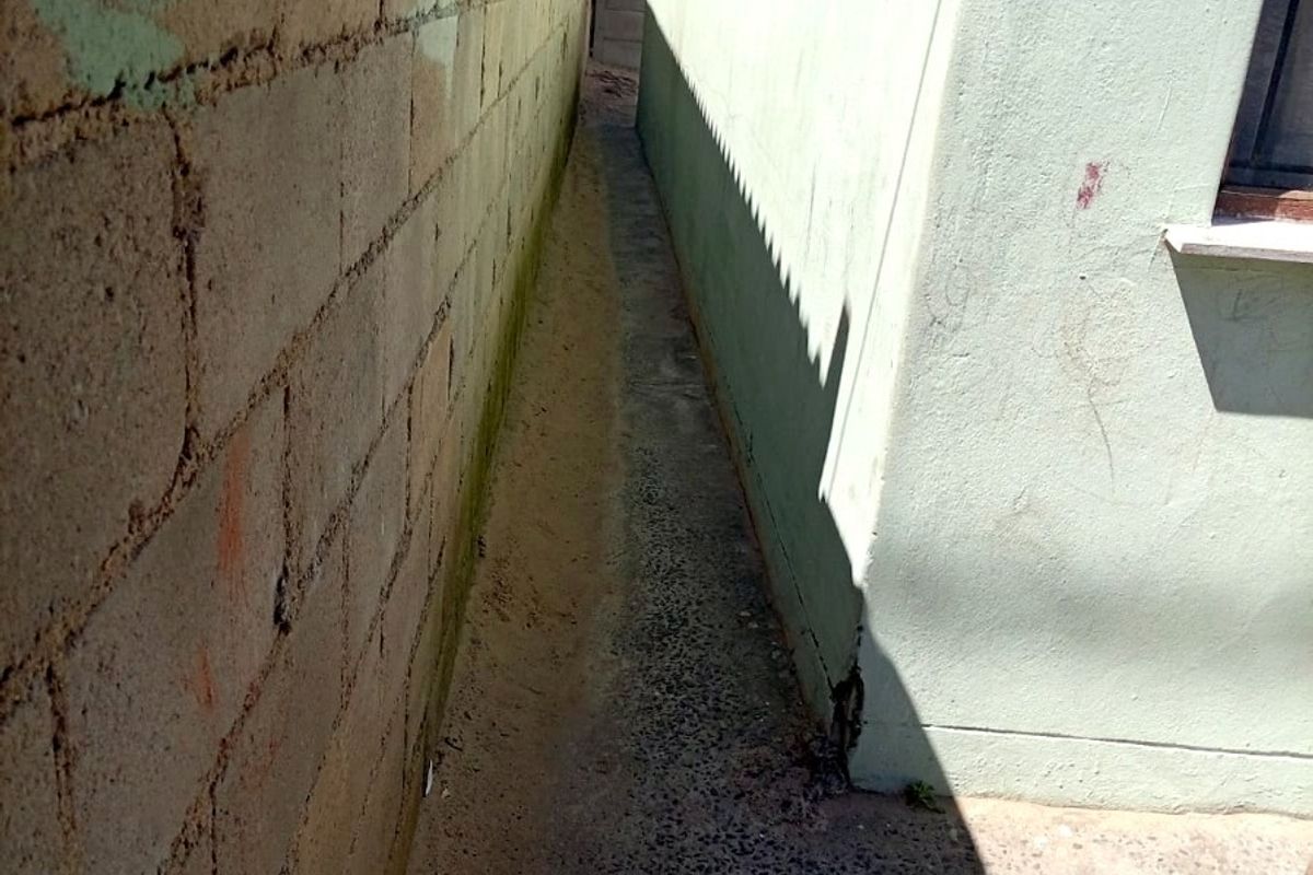 A narrow side passage between the house exterior wall and a concrete boundary wall, featuring a concrete pathway.