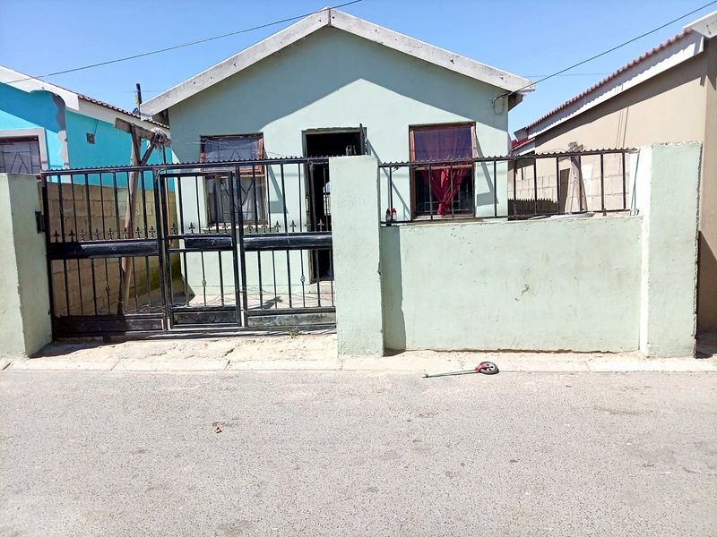 Front elevation of a single-story house featuring a metal security gate, perimeter wall, and tiled roof, showing signs of exterior wear.