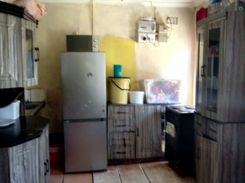 A dated kitchen area featuring fitted cabinetry and tiled flooring, currently requiring cosmetic updates and wall repairs to improve the overall aesthetic.