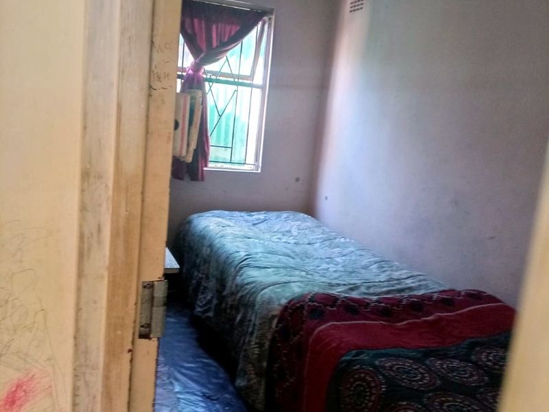 A compact bedroom featuring a window with security bars and basic finishes, requiring cosmetic updates to improve its overall condition and appeal.