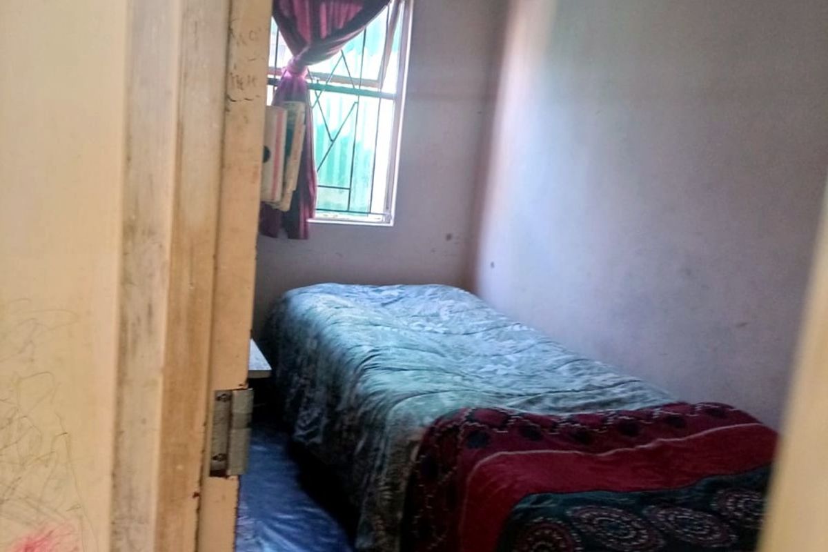 A compact bedroom featuring a window with security bars and basic finishes, requiring cosmetic updates to improve its overall condition and appeal.