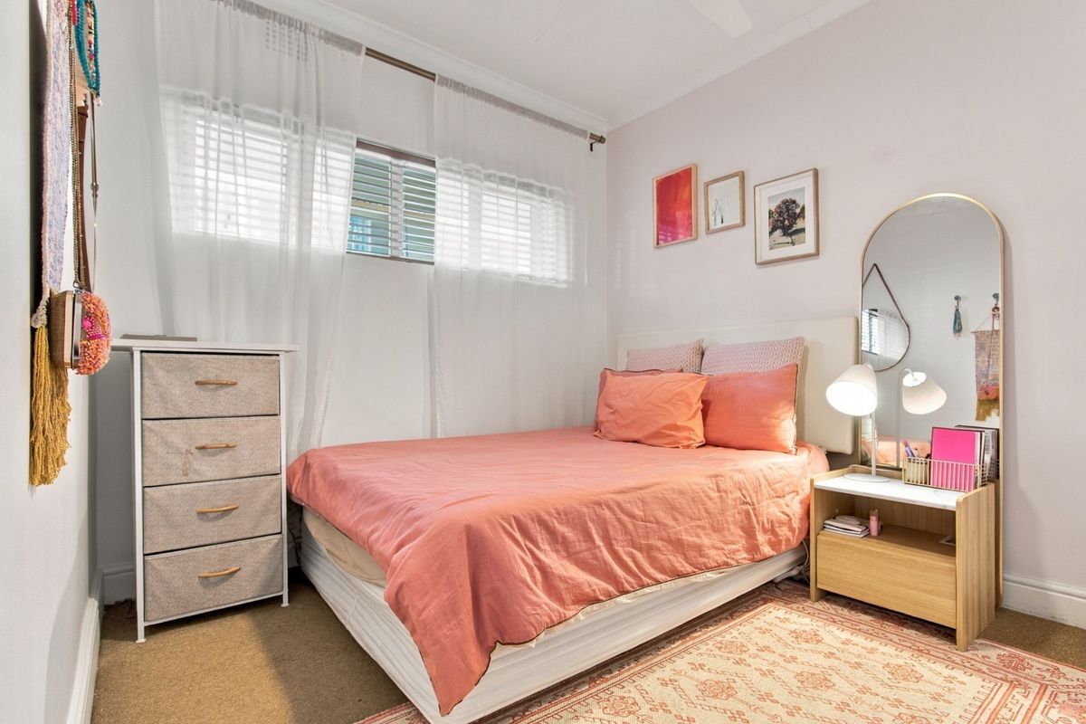 A well-lit bedroom featuring neutral walls, carpeted flooring, and a window with fitted blinds and curtains.