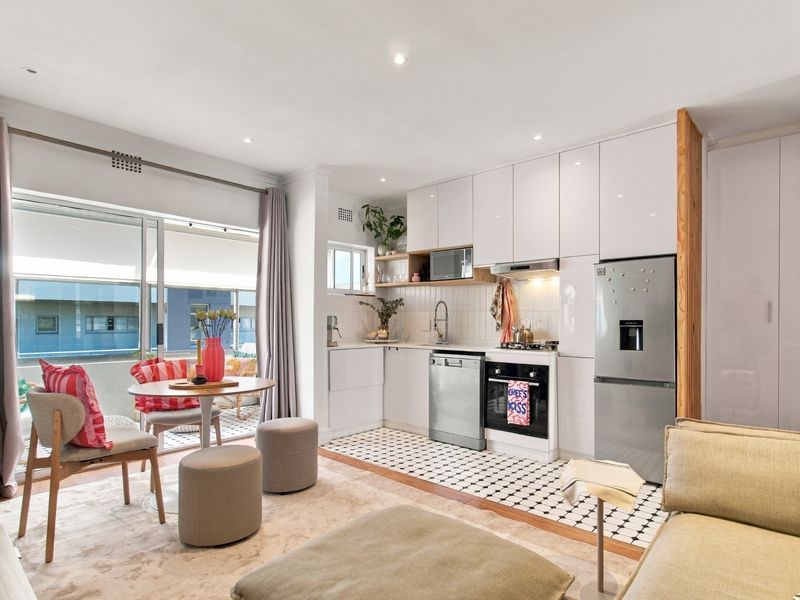 Modern open-plan kitchen and living area featuring sleek white cabinetry, integrated appliances, patterned floor tiles, and direct access to a private balcony.