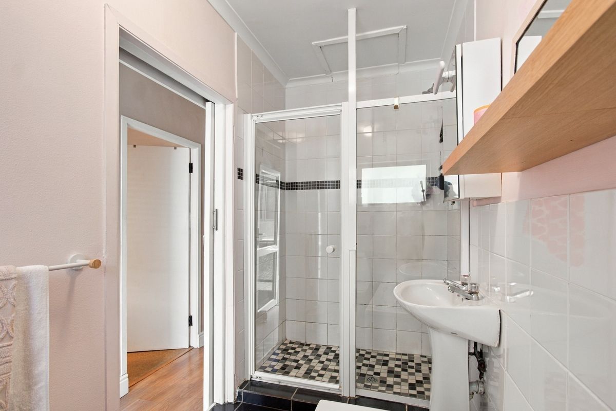 A functional bathroom featuring a pedestal sink, a glass-enclosed shower with tiled walls, and a classic black and white tiled floor.