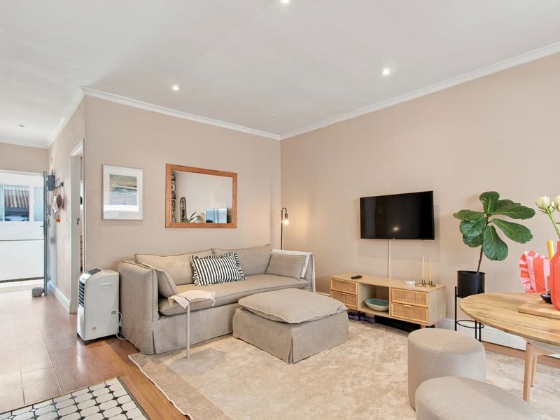 A well-maintained living room featuring laminate flooring, recessed downlighting, and neutral wall finishes, providing a comfortable and inviting space.