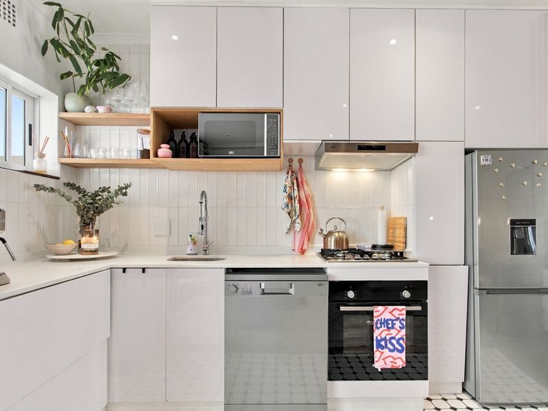 Modern kitchen featuring high-gloss white cabinetry, integrated appliances, gas hob, electric oven, and stylish tiled backsplash with open shelving.
