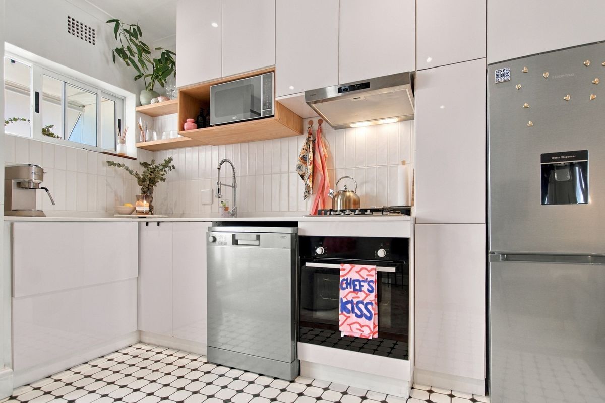 Modern kitchen featuring white high-gloss cabinetry, integrated appliances, a tiled backsplash, and classic patterned floor tiles.