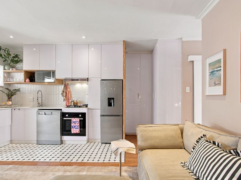 Modern open-plan kitchen featuring sleek white cabinetry, integrated appliances, subway tile backsplash, and a distinct tiled floor area, seamlessly flowing into the living space.