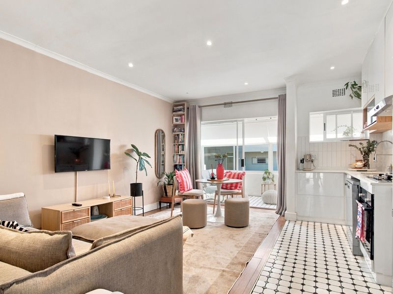Modern open-plan living area featuring a sleek kitchen with built-in appliances, tiled flooring, and seamless access to a private balcony through sliding glass doors.