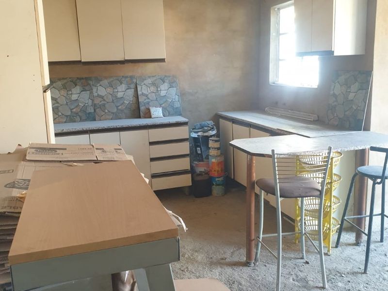 A kitchen space in need of significant renovation, featuring basic cabinetry, tiled splashbacks, and unfinished wall and floor surfaces.