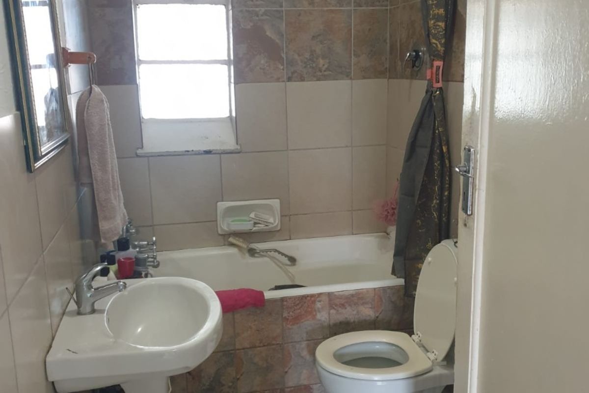Compact bathroom featuring a pedestal basin, built-in bathtub with shower attachment, and toilet, finished with dated wall and floor tiling.