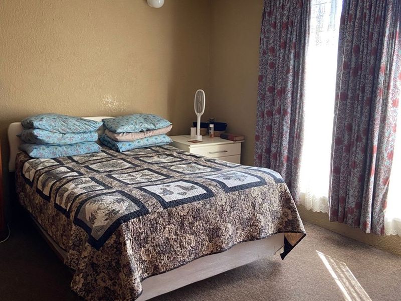 A standard bedroom featuring carpeted flooring, coved ceilings, and a wall-mounted light fixture, offering a functional space with neutral wall tones.