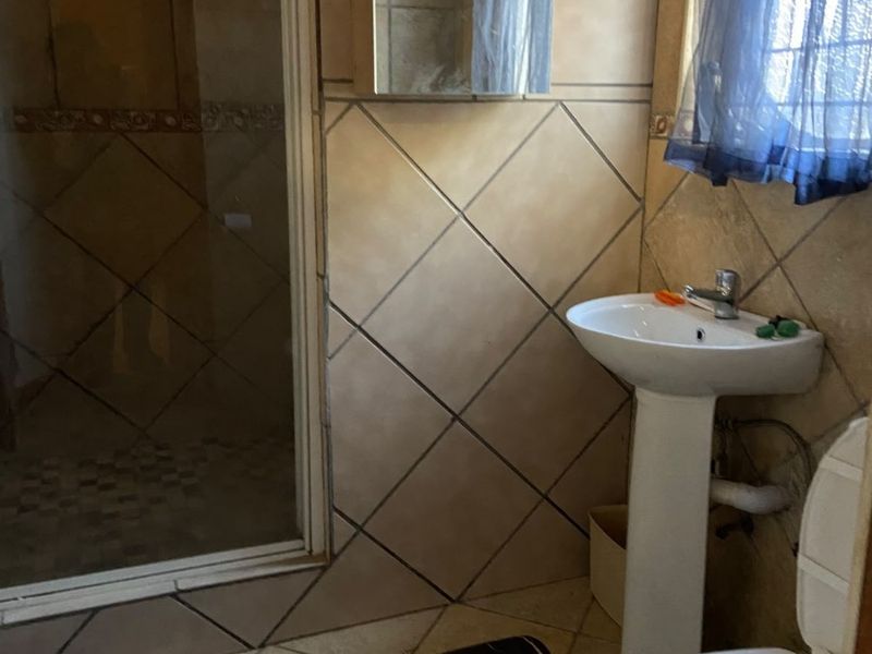 A functional bathroom featuring a pedestal basin, toilet, and a glass-enclosed shower with neutral tiled finishes.