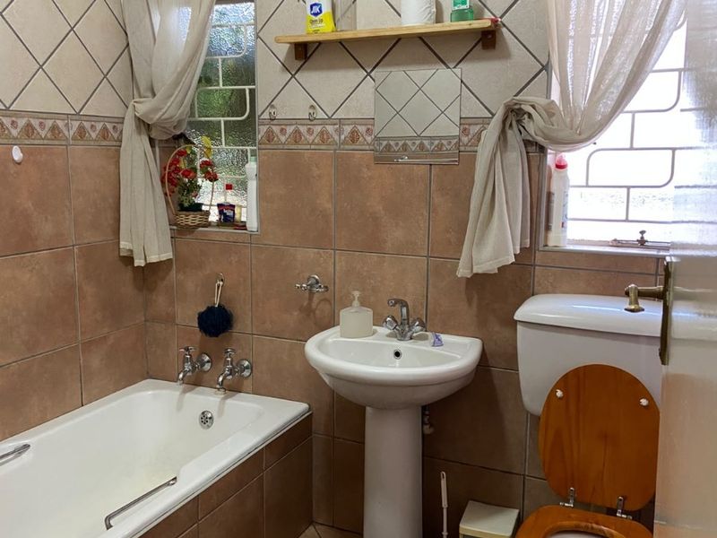 A functional bathroom featuring a bathtub, pedestal basin, and toilet with tiled wall finishes and natural light from two windows.