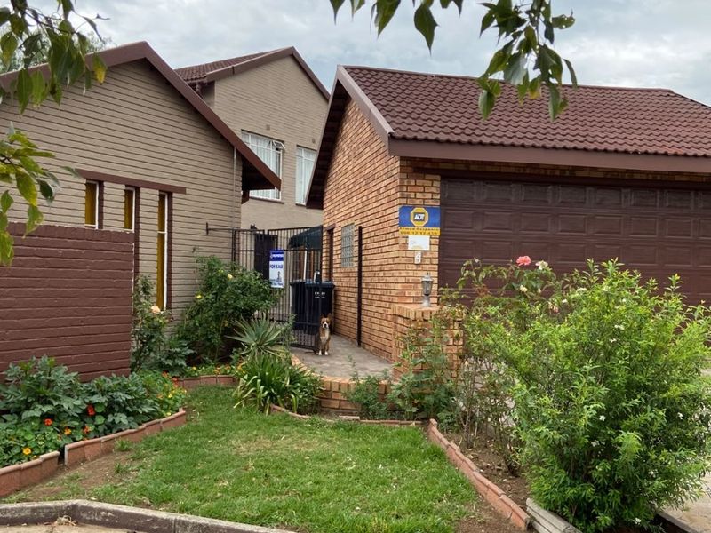 Front exterior view of a residential property featuring a brick facade, tiled roof, garage, and established garden beds.