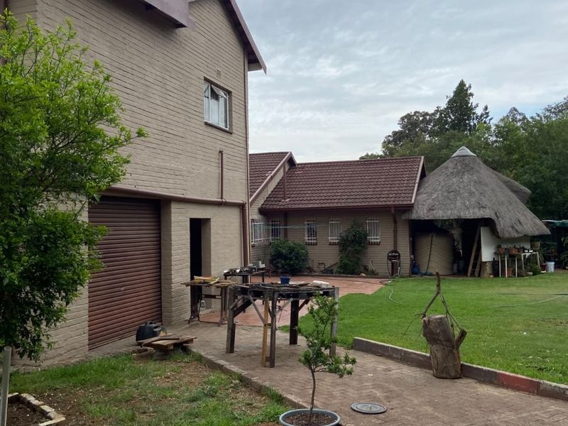 Rear exterior view of the property featuring a brick facade, roller garage door, paved driveway, and a traditional thatched lapa in the garden.