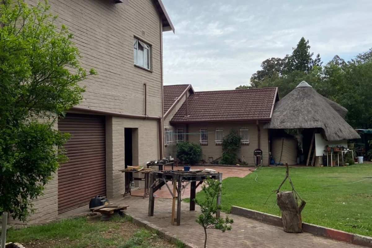Rear exterior view of the property featuring a brick facade, roller garage door, paved driveway, and a traditional thatched lapa in the garden.