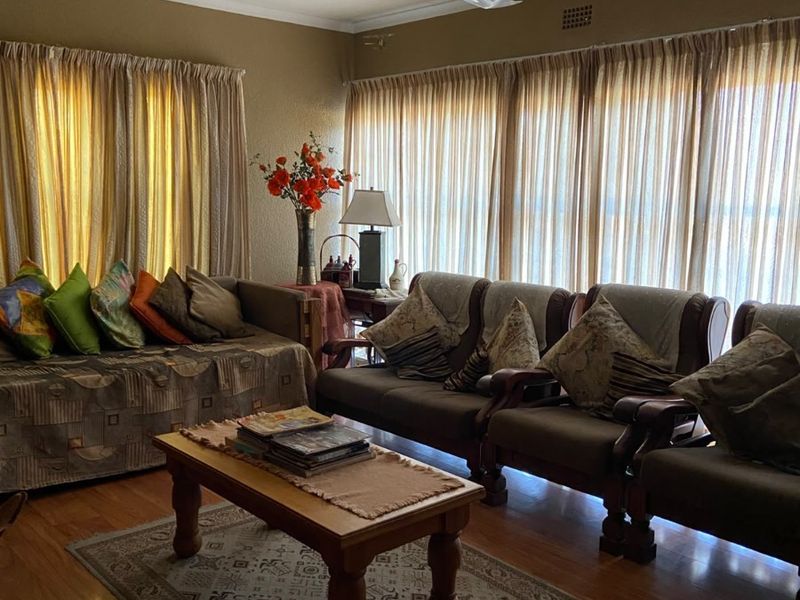 A comfortable living room featuring laminate flooring, a ceiling fan, and large windows with curtains, providing a warm and inviting atmosphere.