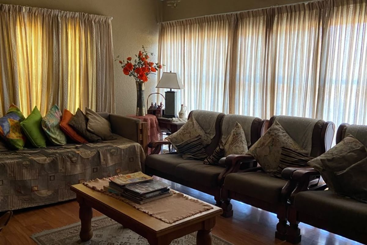 A comfortable living room featuring laminate flooring, a ceiling fan, and large windows with curtains, providing a warm and inviting atmosphere.