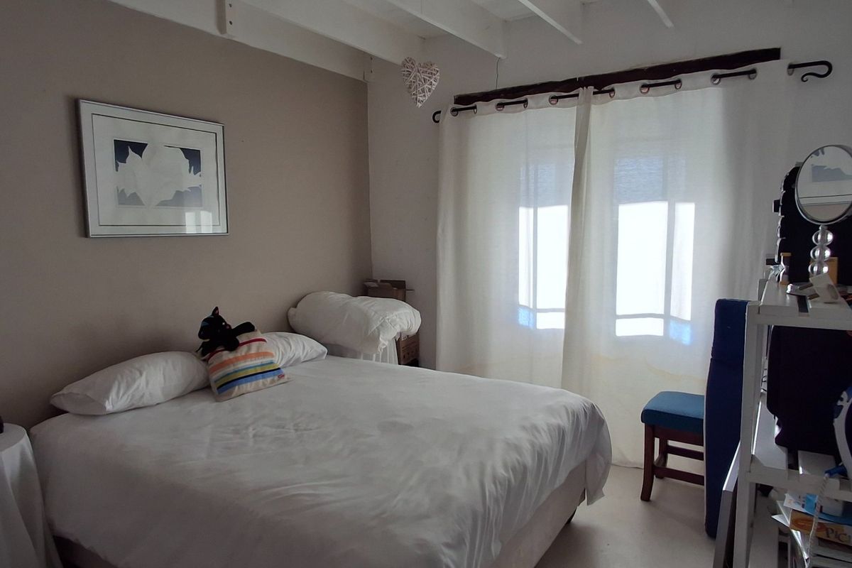 A cozy bedroom featuring exposed ceiling beams and natural light through large window curtains.