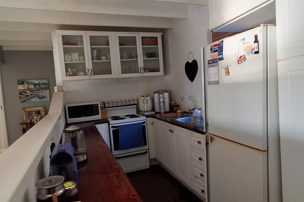 A functional kitchen featuring white cabinetry, a freestanding stove, a sink, and exposed ceiling beams, providing a practical workspace with a classic aesthetic.