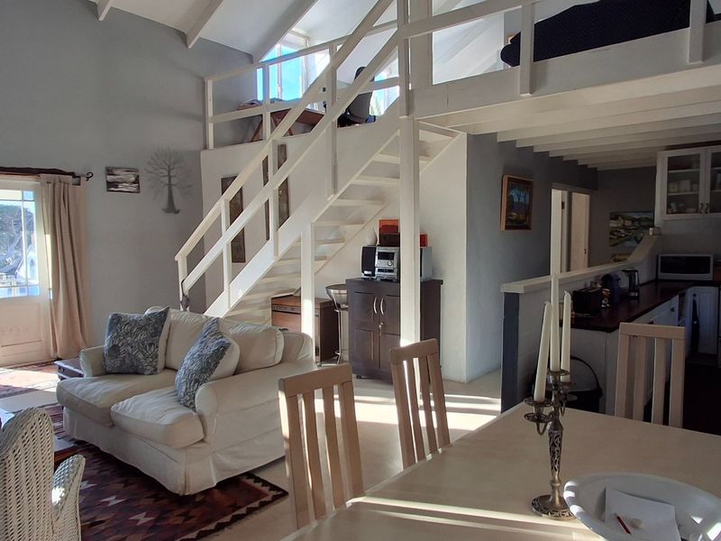 Open-plan living and dining area featuring a vaulted ceiling, mezzanine level with timber staircase, and direct access to an outdoor patio.