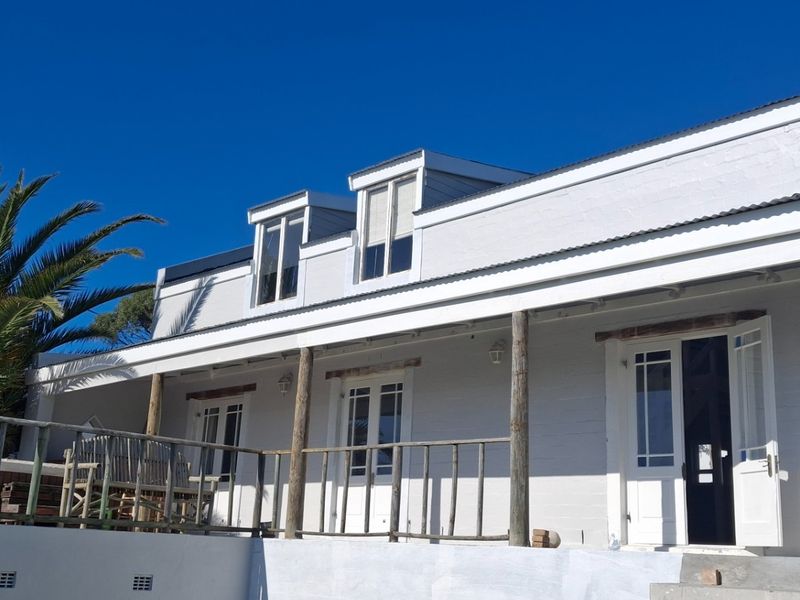 Rear elevation of a white painted brick house featuring a covered patio with timber posts and dormer windows under a clear blue sky.