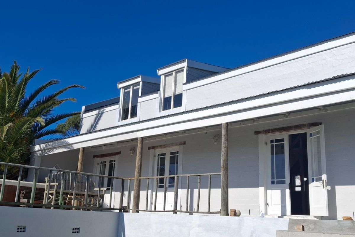 Rear elevation of a white painted brick house featuring a covered patio with timber posts and dormer windows under a clear blue sky.