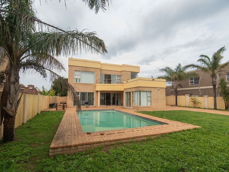 Rear view of a two-story brick house featuring a swimming pool, paved surround, and a private garden with boundary walls.