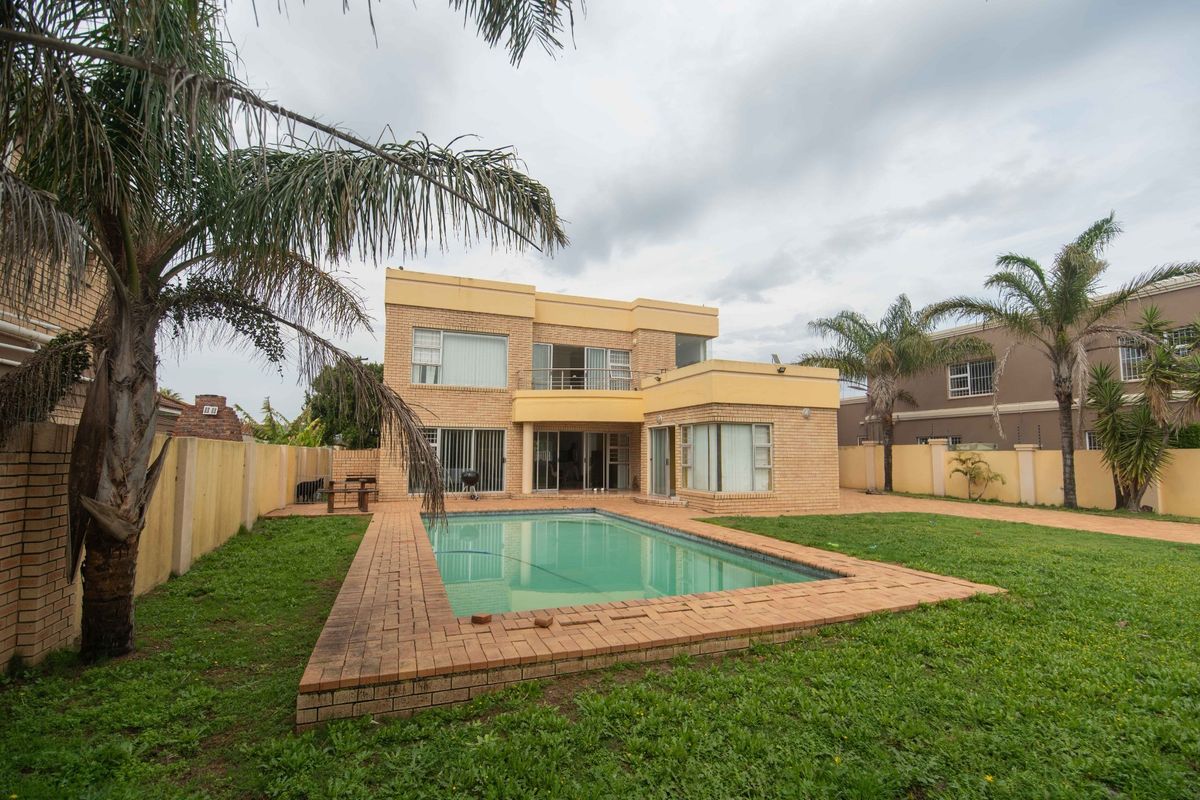 Rear view of a two-story brick house featuring a swimming pool, paved surround, and a private garden with boundary walls.