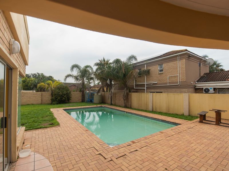 Outdoor pool area featuring a swimming pool, brick paved surround, and perimeter boundary walls, viewed from a covered patio.