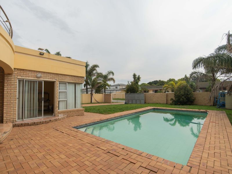 Rear exterior view featuring a swimming pool, brick paved patio area, and a brick boundary wall.