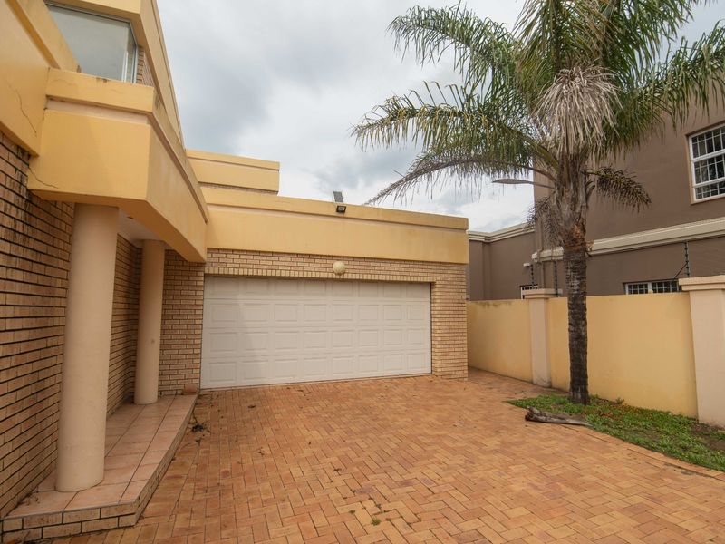 Front exterior view of the property featuring a brick driveway, double garage, and covered entrance area with perimeter walling.